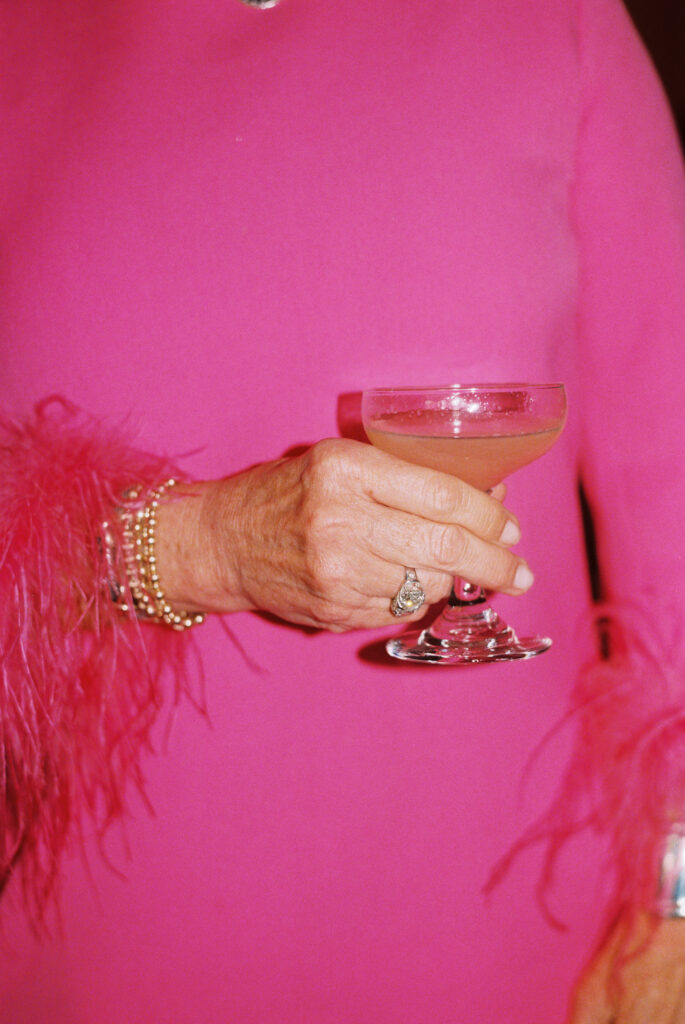 wedding guest dressed up in hot pink with feathers and diamonds holding martini glass at wedding reception