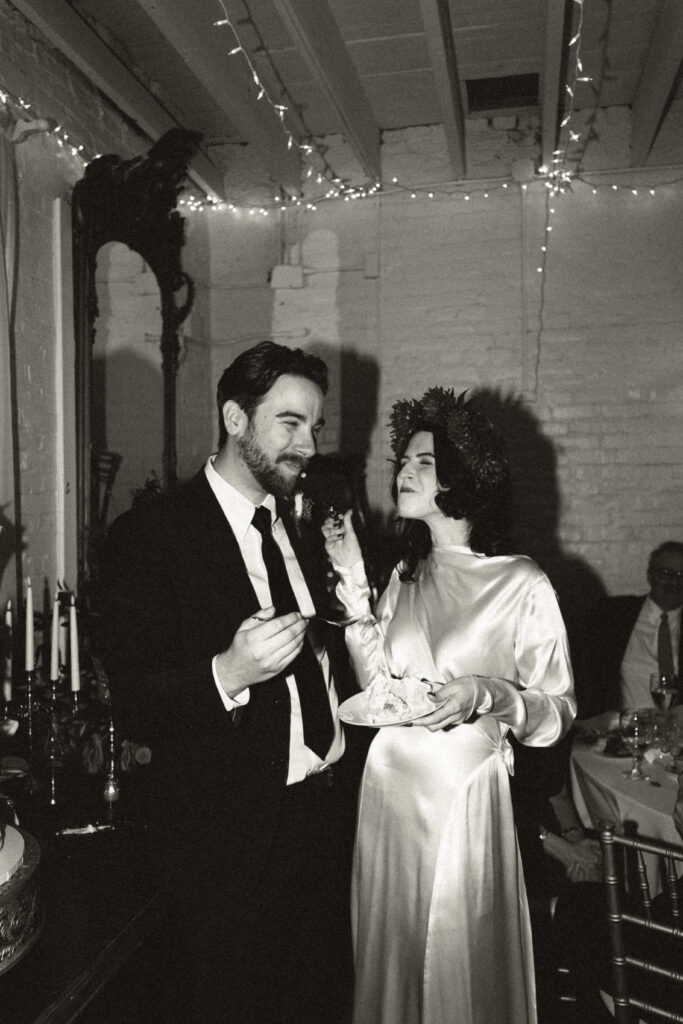 Wedding couple bride and groom sharing sweet moment after tasting wedding cake together in black and white film 