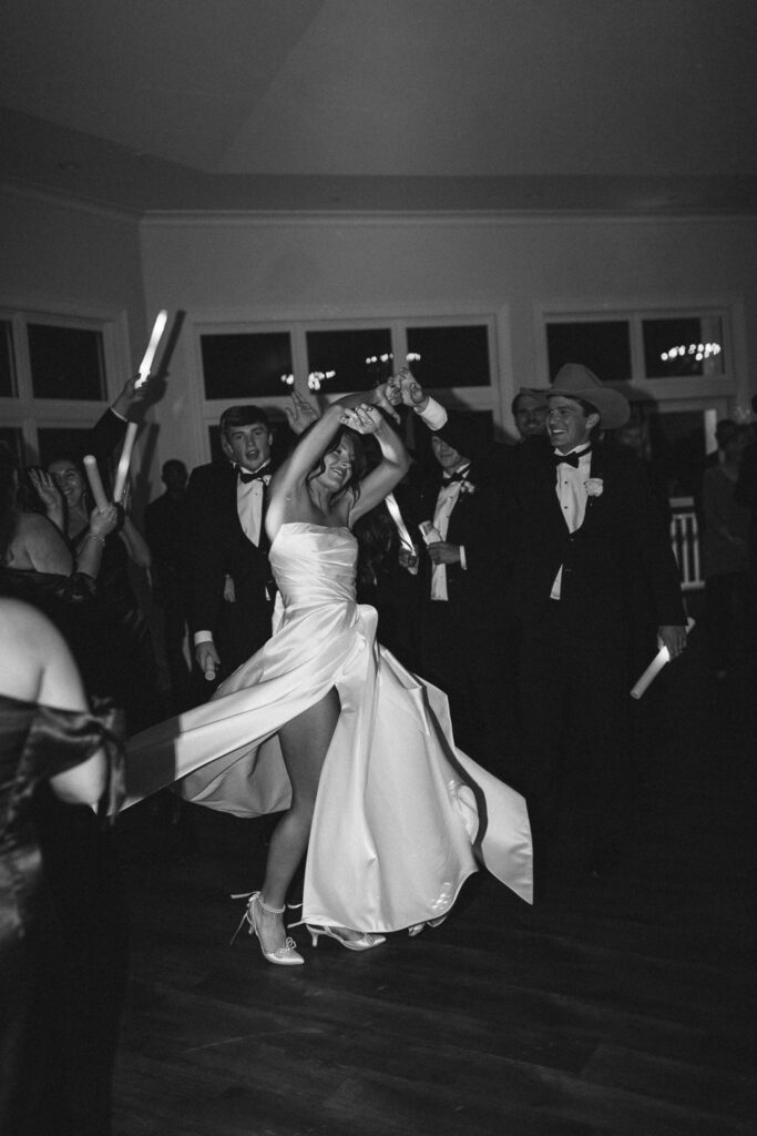 Wedding guests on dance floor in black and white with groom spinning bride in wedding dress with high slit
