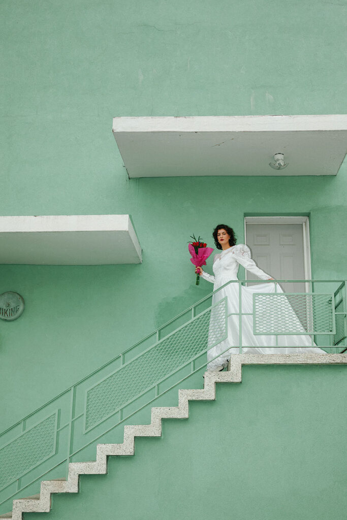 bride walking down art deco style stairs in vintage wedding dress with bright pink florals